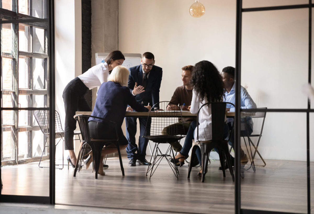 Diverse employees team engaged in teamwork in modern boardroom, sitting at table in office, reading legal documents, analyzing project statistics, financial report, discussing strategy, planning